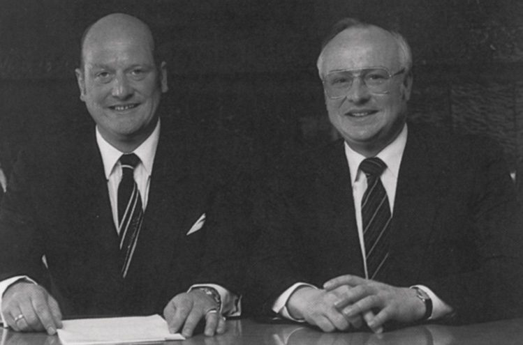 Helmut und Erich Kropf am Schreibtisch, beide im dunklen Anzug.